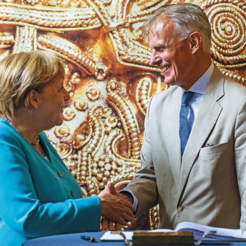 Friis Arne Petersen, der gennem de seneste fem år har været tæt på tysk politik som dansk ambassadør i Berlin, en stilling han forlader 1. september, hilser her på Angela Merkel i 2019 på Stralsund Museum i Mecklenburg-Vorpommern på en udstilling om vikingeguld tilskrevet Harald Blåtand.