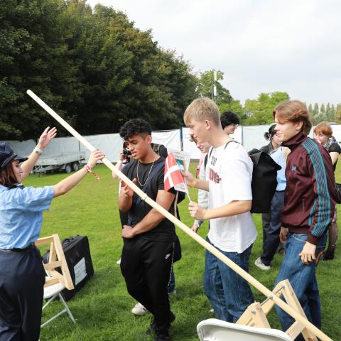 Kulturmødeambassadør Nesrin åbner grænsebommen for en gruppe drenge fra Mulernes Legatskole, Odense, der med otte korrekte svar ud af ti mulige klarede grænsekontrollen ved Grænseforeningens stand i Mangfoldighedsteltet på Ungdommens Folkemøde i Valbyparken den 8.-9. september.