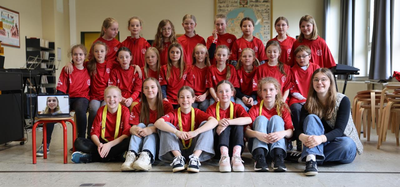 Lisa Stammer sammen med børnekoret på Hiort Lorenzen Skolen i Slesvig, som synger kor på ‘Vor Sang’. Nike Engels er med på en videoforbindelse på en computer til venstre.