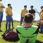 Træner Nils Jacobsen, med solbriller, gennemgår taktikken forud for dagens kamp. 